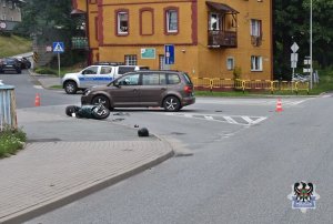 Zdjęcie przedstawia skrzyżowanie, na którym stoi radiowóz oraz samochód osobowy. Po lewej stronie leży rozbity motorower