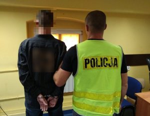 Zdjęcie przedstawia dwie osoby, sprawcę kradzieży oraz policjanta w kamizelce odblaskowej, którzy stoją tyłem