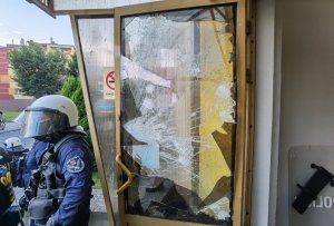 Policjant w mundurze stoi przy uszkodzonych drzwiach wejściowych do Komendy Powiatowej Policji w Lubinie
