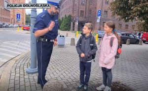 Policjant rozmawia z dziećmi przed przejściem dla pieszych