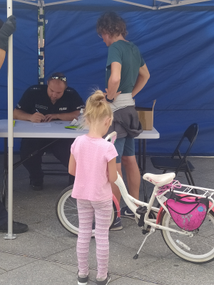policjant notuje w rejestrze dane, widać dziewczynkę i kobietę, które przyszły oznakować rower